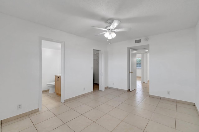 unfurnished bedroom featuring ensuite bathroom, ceiling fan, a spacious closet, light tile patterned floors, and a closet