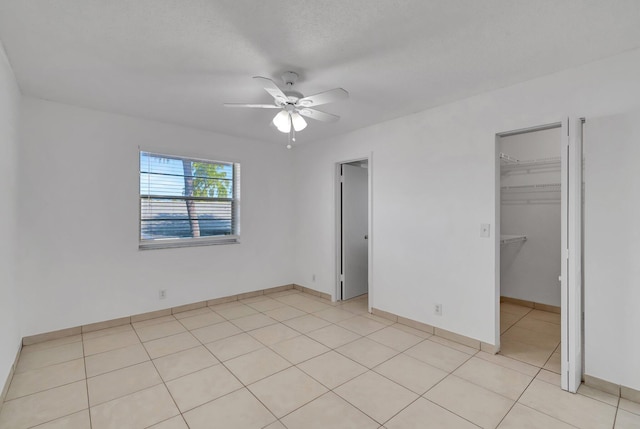 unfurnished bedroom with ceiling fan, a walk in closet, light tile patterned floors, and a closet