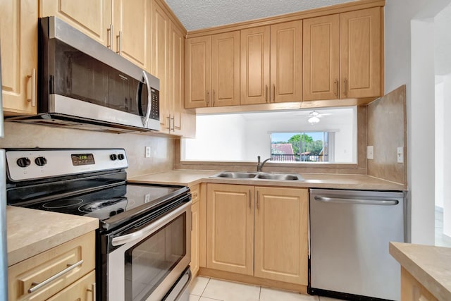 kitchen with appliances with stainless steel finishes, light brown cabinetry, a textured ceiling, sink, and light tile patterned flooring