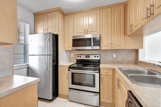 kitchen featuring a textured ceiling, stainless steel appliances, sink, light tile patterned floors, and light brown cabinets