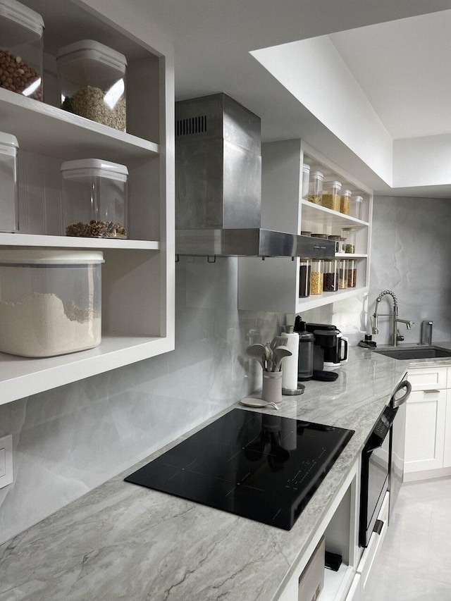 kitchen with wall chimney exhaust hood, light stone countertops, black electric cooktop, sink, and white cabinetry