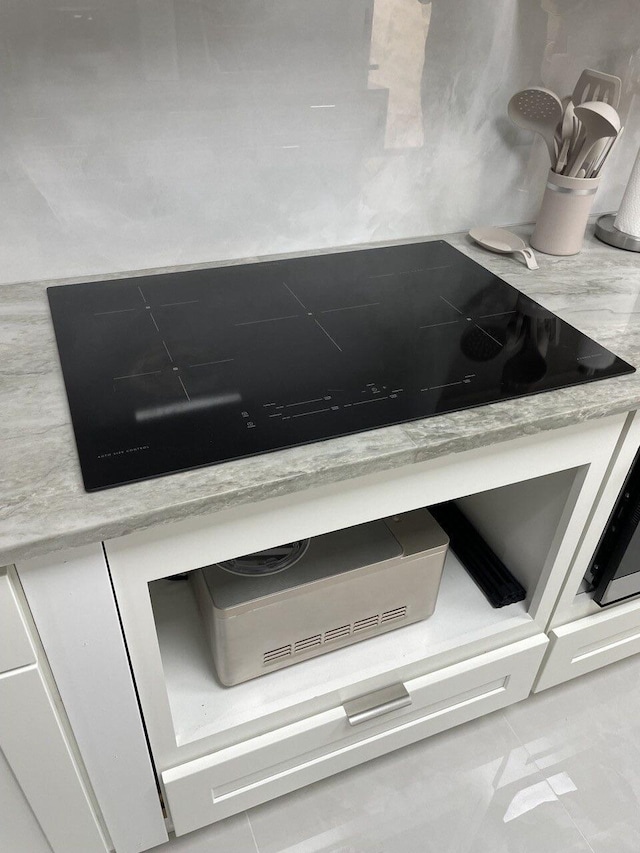 interior details featuring black electric cooktop, white cabinetry, and backsplash