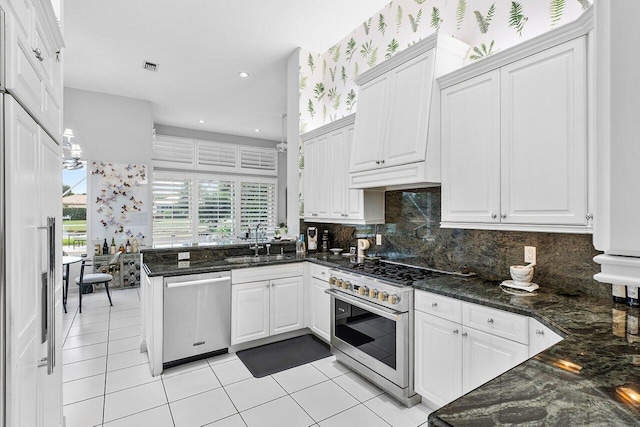 kitchen featuring light tile patterned floors, white cabinetry, stainless steel appliances, dark stone counters, and sink