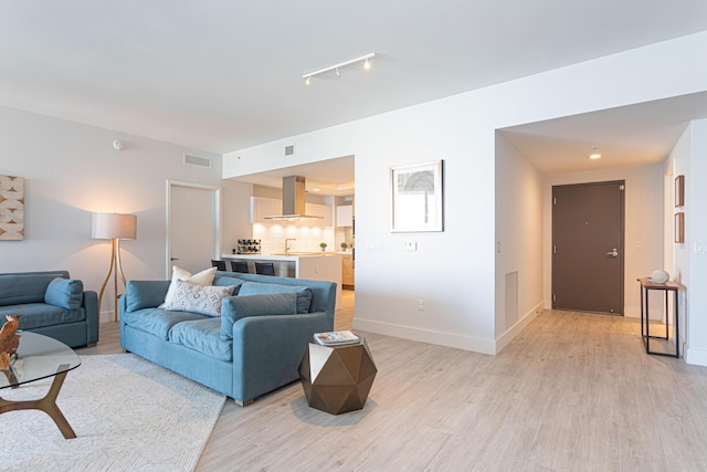 living room featuring sink, light wood-type flooring, and rail lighting