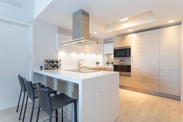 kitchen featuring kitchen peninsula, island range hood, oven, a breakfast bar area, and black microwave