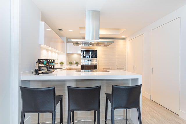 kitchen featuring a kitchen breakfast bar, light hardwood / wood-style flooring, island range hood, and kitchen peninsula