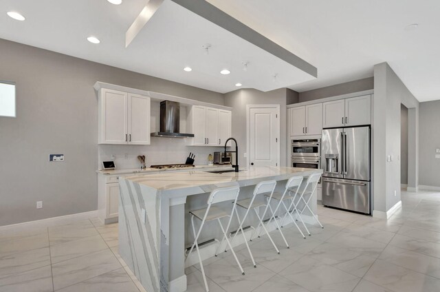 kitchen featuring a center island with sink, sink, white cabinetry, stainless steel appliances, and wall chimney exhaust hood