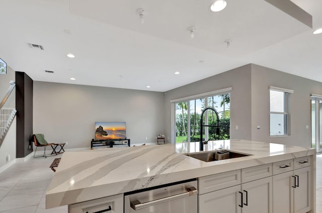 kitchen featuring white cabinetry, a kitchen island with sink, light stone countertops, stainless steel dishwasher, and sink