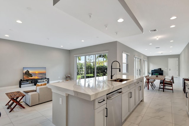 kitchen featuring sink, a center island with sink, and light stone countertops