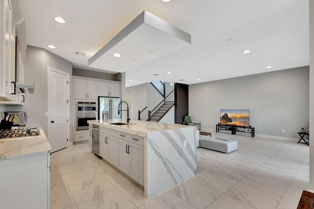 kitchen featuring white cabinetry, an island with sink, stainless steel appliances, light stone counters, and sink