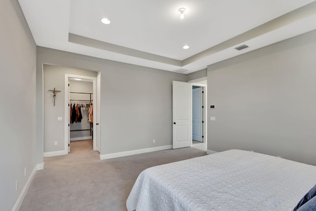 carpeted bedroom featuring a walk in closet, a closet, and a tray ceiling