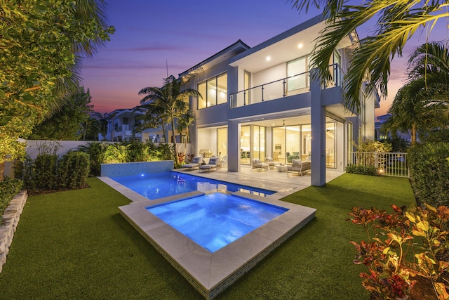 pool at dusk featuring an in ground hot tub, outdoor lounge area, a lawn, and a patio area