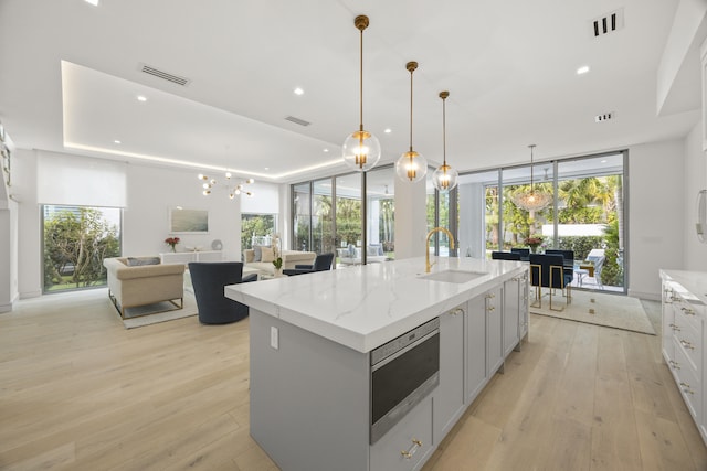 kitchen featuring light hardwood / wood-style flooring, decorative light fixtures, sink, light stone counters, and a center island with sink