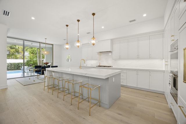 kitchen with a large island with sink, white cabinets, decorative light fixtures, a wall of windows, and tasteful backsplash