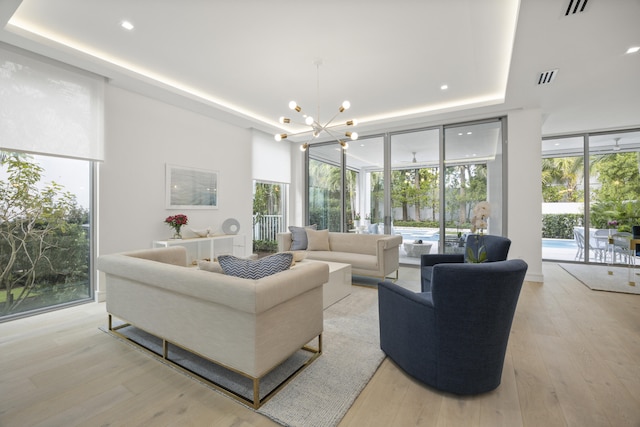 living room featuring a wall of windows, ceiling fan with notable chandelier, and light hardwood / wood-style flooring