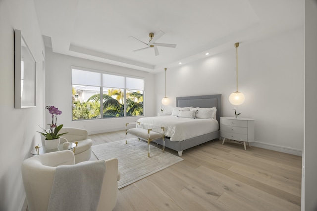 bedroom with a raised ceiling, ceiling fan, and light hardwood / wood-style floors