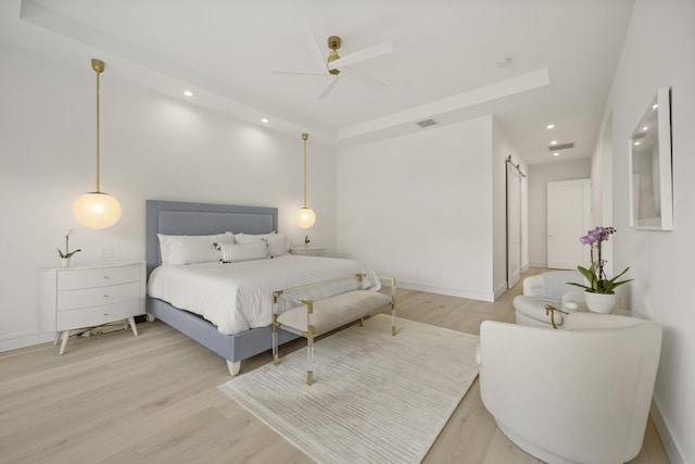 bedroom featuring a raised ceiling, a barn door, ceiling fan, and light hardwood / wood-style floors