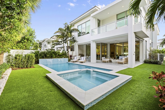 back of house featuring an outdoor hangout area, a pool with hot tub, a lawn, and a balcony