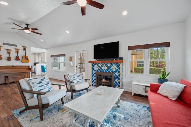 living room with dark wood-type flooring, a tiled fireplace, vaulted ceiling, and ceiling fan