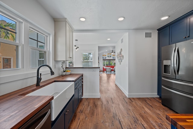 kitchen featuring wooden counters, blue cabinets, appliances with stainless steel finishes, wood-type flooring, and sink