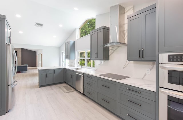 kitchen with gray cabinetry, wall chimney range hood, sink, vaulted ceiling, and appliances with stainless steel finishes