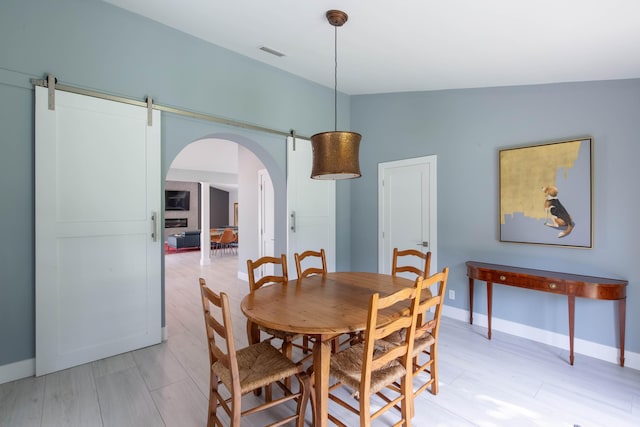 dining space with a barn door, light hardwood / wood-style floors, and lofted ceiling