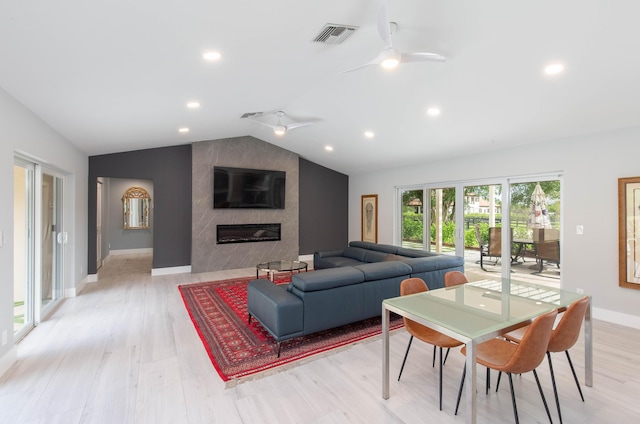 living room with ceiling fan, a large fireplace, light wood-type flooring, and vaulted ceiling