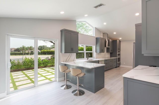 kitchen with backsplash, wall chimney range hood, sink, gray cabinets, and kitchen peninsula