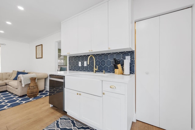 kitchen with backsplash, white cabinets, sink, light hardwood / wood-style flooring, and stainless steel dishwasher