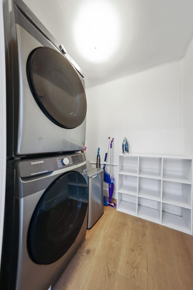 clothes washing area with light hardwood / wood-style flooring and stacked washer / drying machine