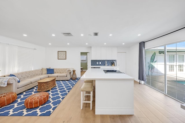 kitchen with decorative backsplash, a kitchen breakfast bar, light wood-type flooring, a kitchen island, and white cabinetry