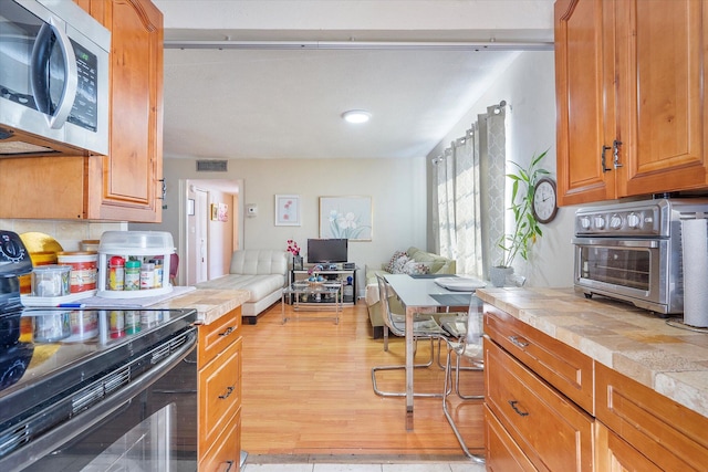 kitchen with black electric range oven, tile countertops, and light hardwood / wood-style floors