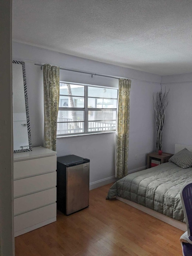 bedroom featuring stainless steel refrigerator, a textured ceiling, and hardwood / wood-style flooring