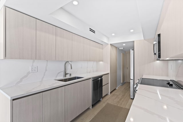 kitchen with sink, light hardwood / wood-style flooring, light stone counters, and appliances with stainless steel finishes