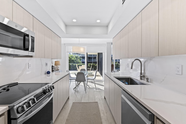 kitchen featuring pendant lighting, light hardwood / wood-style floors, backsplash, appliances with stainless steel finishes, and sink