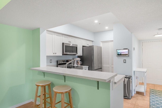 kitchen featuring white cabinets, a breakfast bar area, light tile patterned floors, kitchen peninsula, and stainless steel appliances