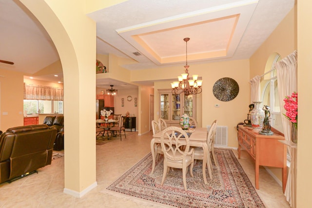 tiled dining room with ceiling fan with notable chandelier and a raised ceiling