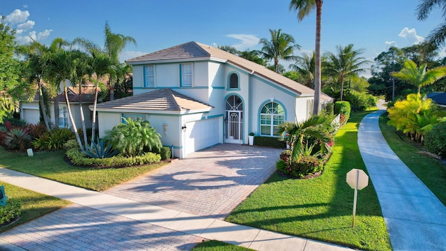 mediterranean / spanish-style home with decorative driveway, a front lawn, an attached garage, and stucco siding