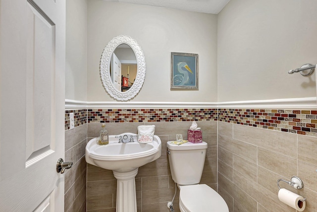 half bath featuring a wainscoted wall, toilet, and tile walls