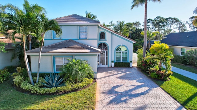 view of front of home featuring stucco siding, a tiled roof, decorative driveway, and a front lawn