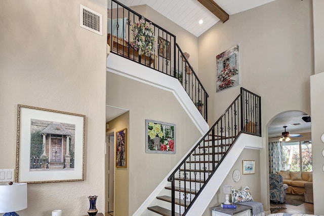 stairway with visible vents, baseboards, ceiling fan, beam ceiling, and a towering ceiling