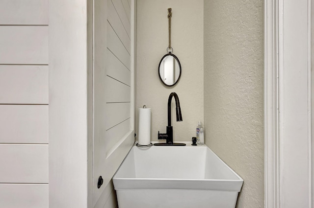 details featuring a freestanding tub, a textured wall, and a sink