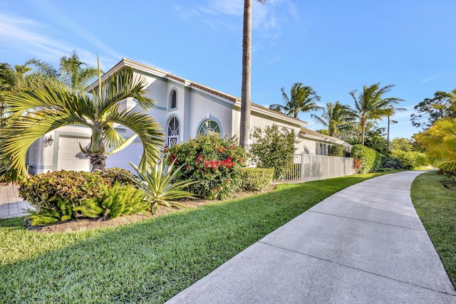 view of property exterior with stucco siding, a lawn, an attached garage, and fence