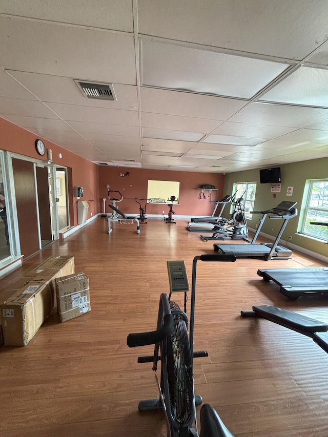 exercise room featuring baseboards, visible vents, a drop ceiling, and wood finished floors