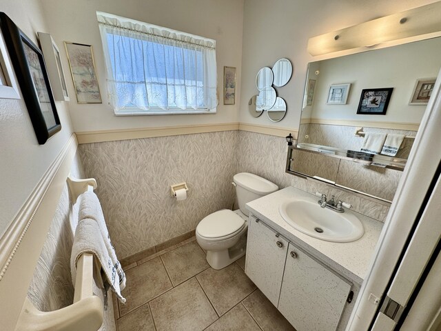 half bathroom with toilet, wainscoting, vanity, and tile patterned floors