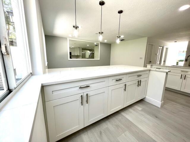 kitchen featuring light stone countertops, kitchen peninsula, decorative light fixtures, light hardwood / wood-style flooring, and white cabinetry