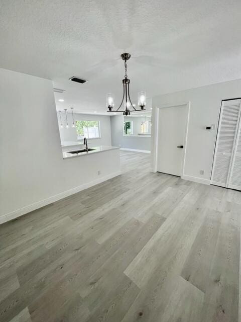 unfurnished living room with a textured ceiling, an inviting chandelier, light hardwood / wood-style flooring, and sink