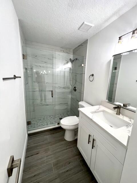 bathroom featuring vanity, a textured ceiling, toilet, and a shower with shower door