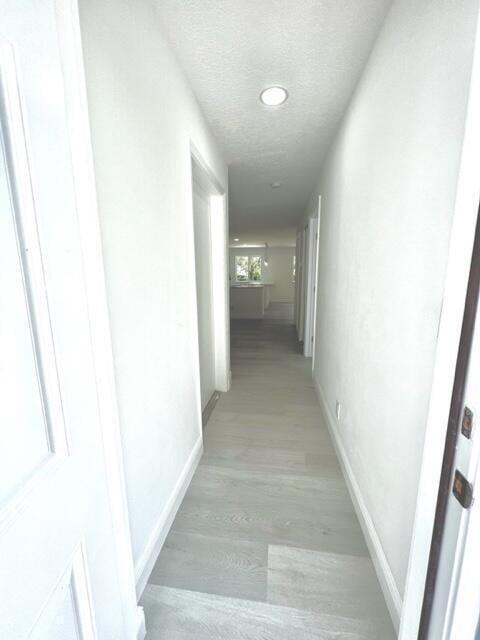 hallway with light hardwood / wood-style floors and a textured ceiling