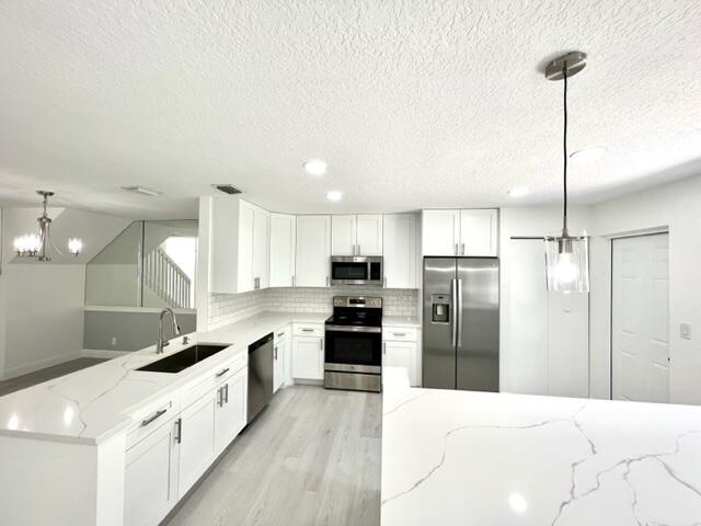 kitchen featuring light stone countertops, sink, stainless steel appliances, decorative light fixtures, and white cabinets